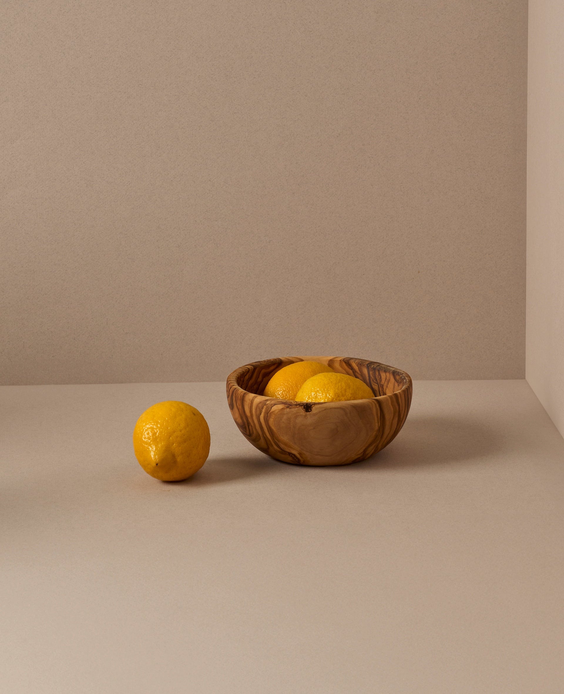 A set of natural olive wood bowls in various sizes, with the smallest bowls containing lemons. The bowls display a beautiful wood grain pattern.
