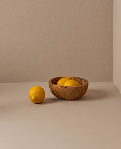 A set of natural olive wood bowls in various sizes, with the smallest bowls containing lemons. The bowls display a beautiful wood grain pattern.