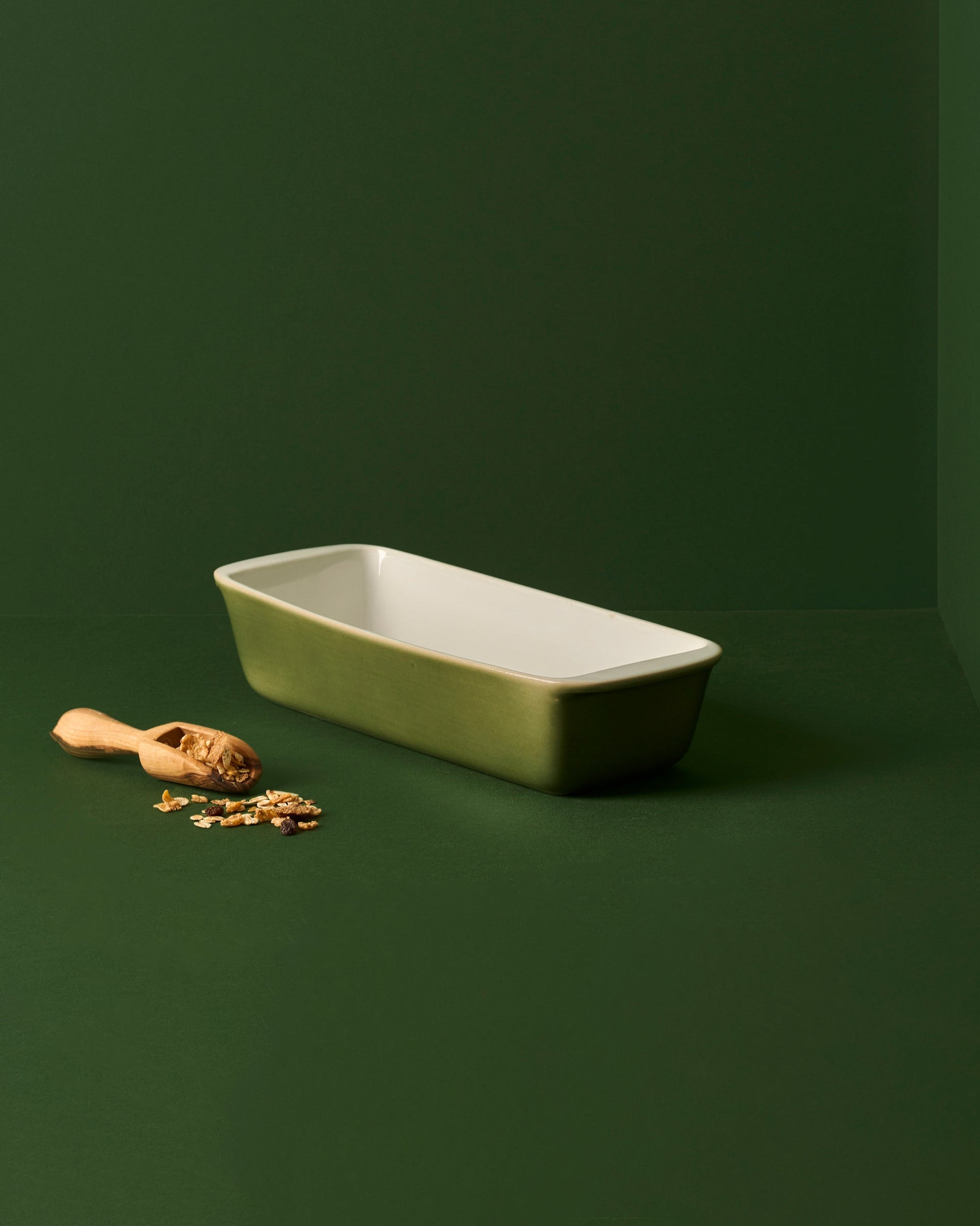 A white enameled stoneware cake and bread pan on a beige background, with two red apples placed on top of it to the side.